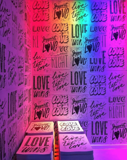 A rainbow lit room with various LGBT love is love posters.